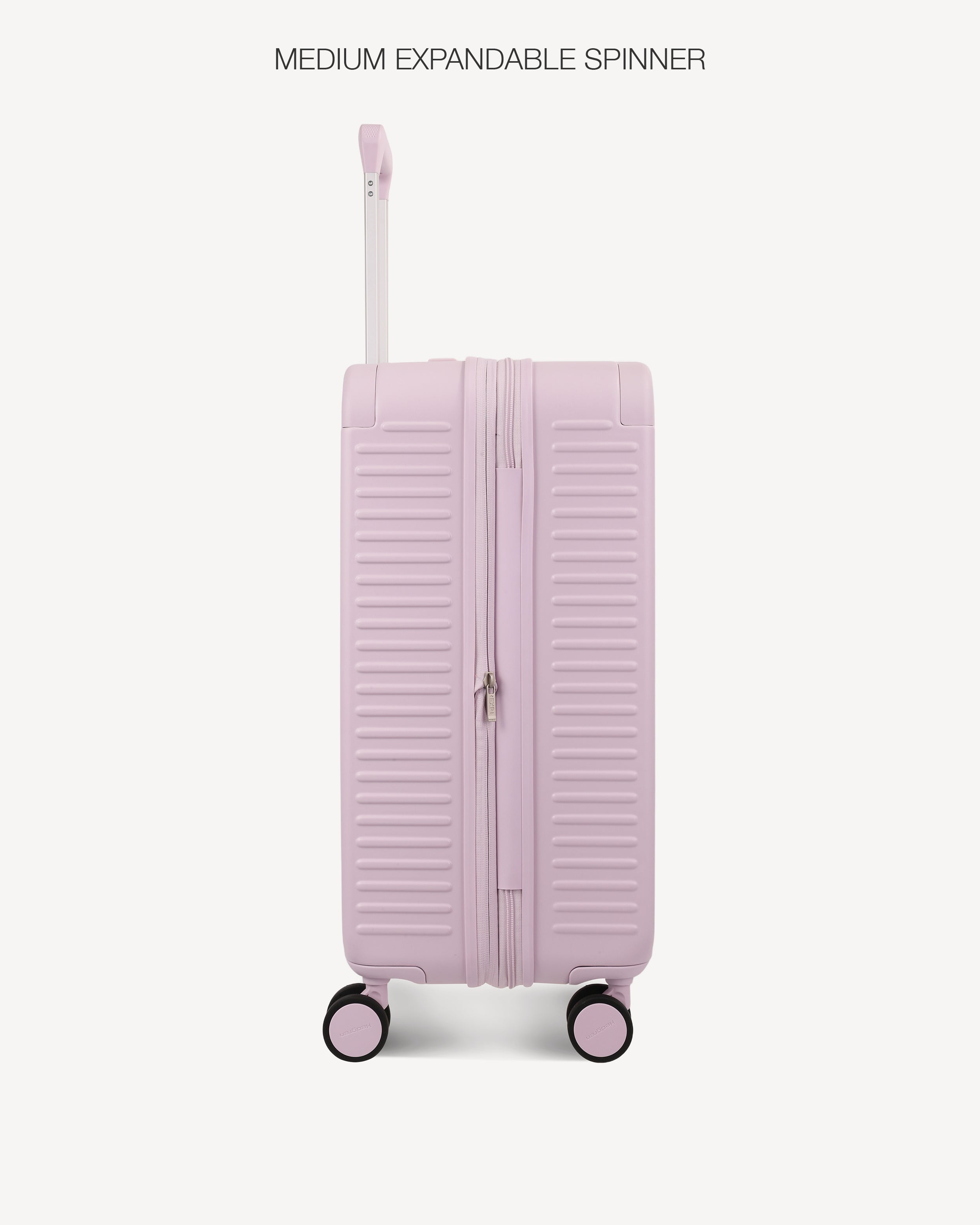 A light pink hard-shell spinner suitcase with a telescoping handle extended, shown against a plain off-white background. Text at the top reads 'MEDIUM EXPANDABLE SPINNER'.