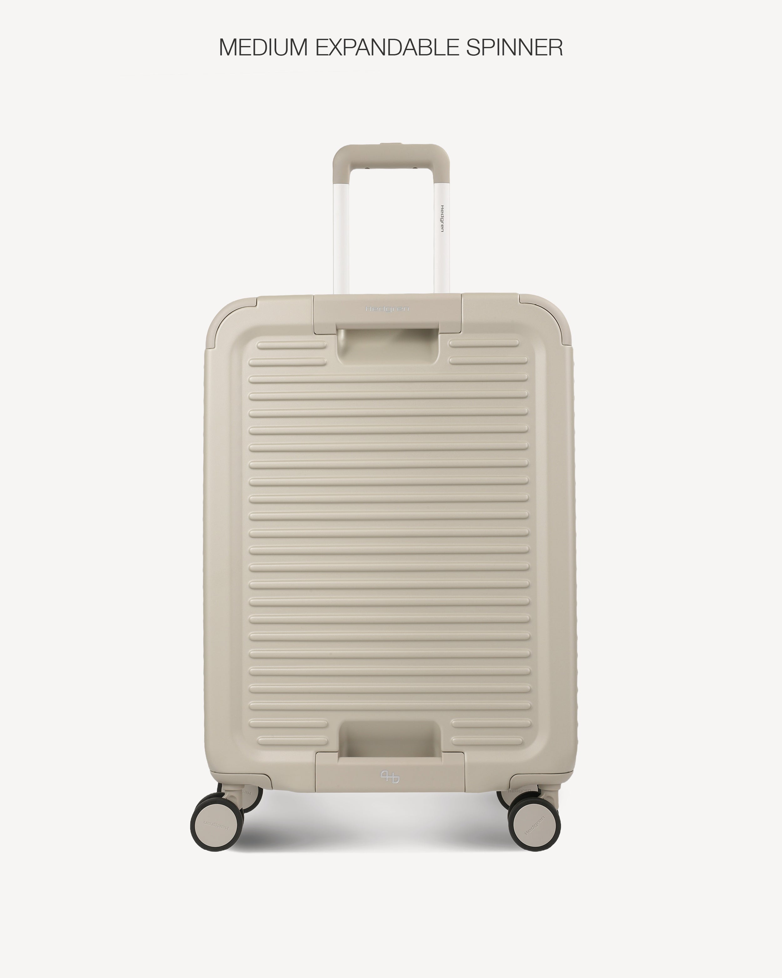 A hard-shell spinner suitcase in a light grey color, featuring a ribbed front design, an extended telescoping handle, and four multi-directional wheels. The text 'MEDIUM EXPANDABLE SPINNER' is printed at the top of the image against a clean, light off-white background.