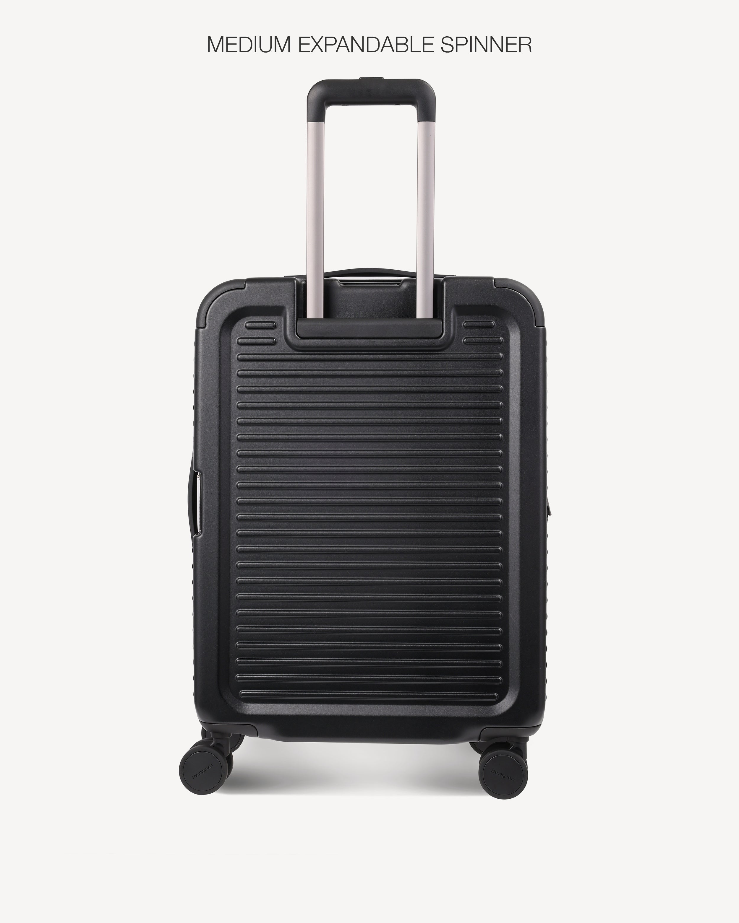 A black hard-shell spinner suitcase with a telescopic handle extended, shown from the back against a light gray background. The text 'MEDIUM EXPANDABLE SPINNER' is printed at the top.