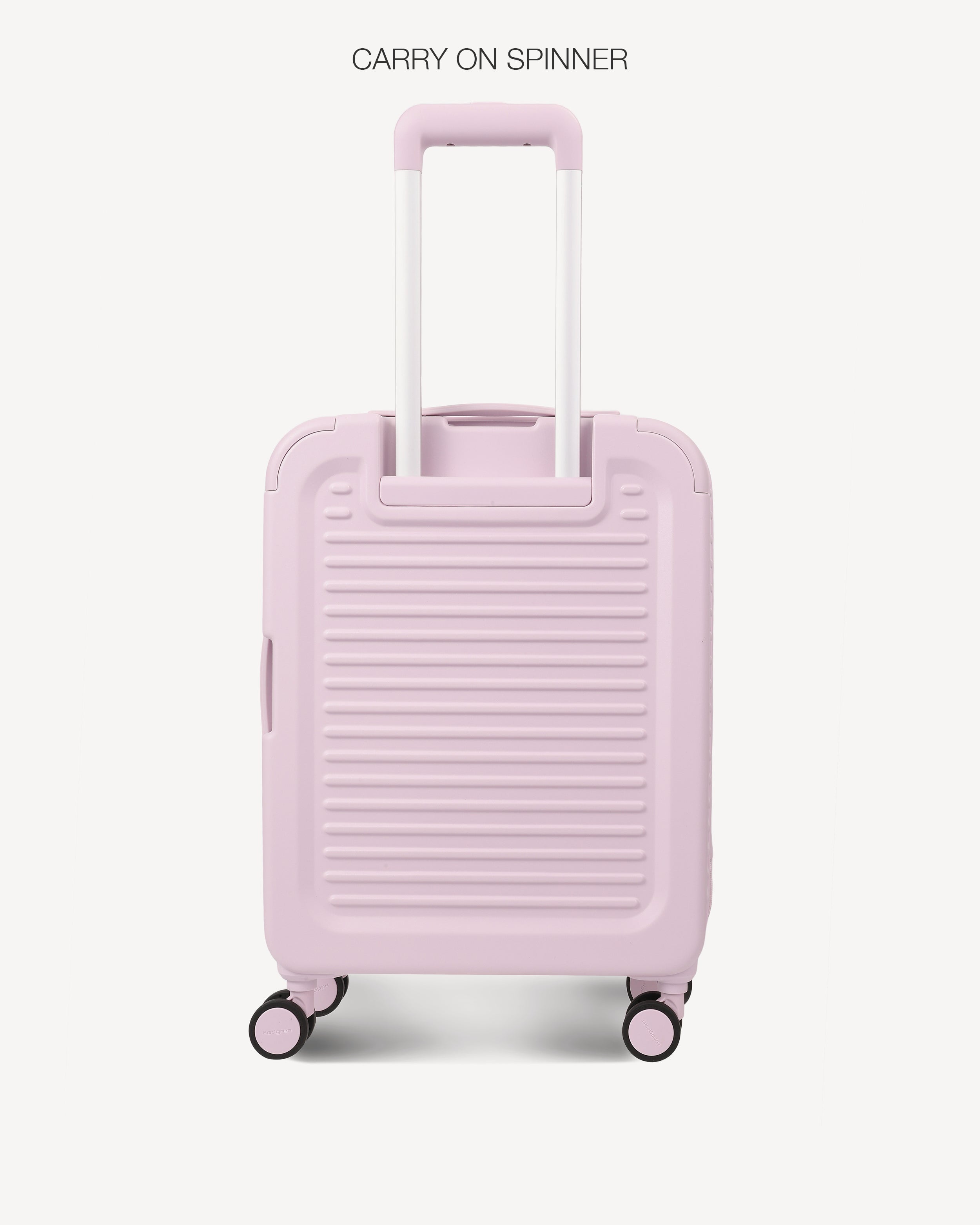 A light pink hard-shell spinner suitcase with a telescopic handle extended, shown against a plain off-white background. The text 'CARRY ON SPINNER' is printed at the top.