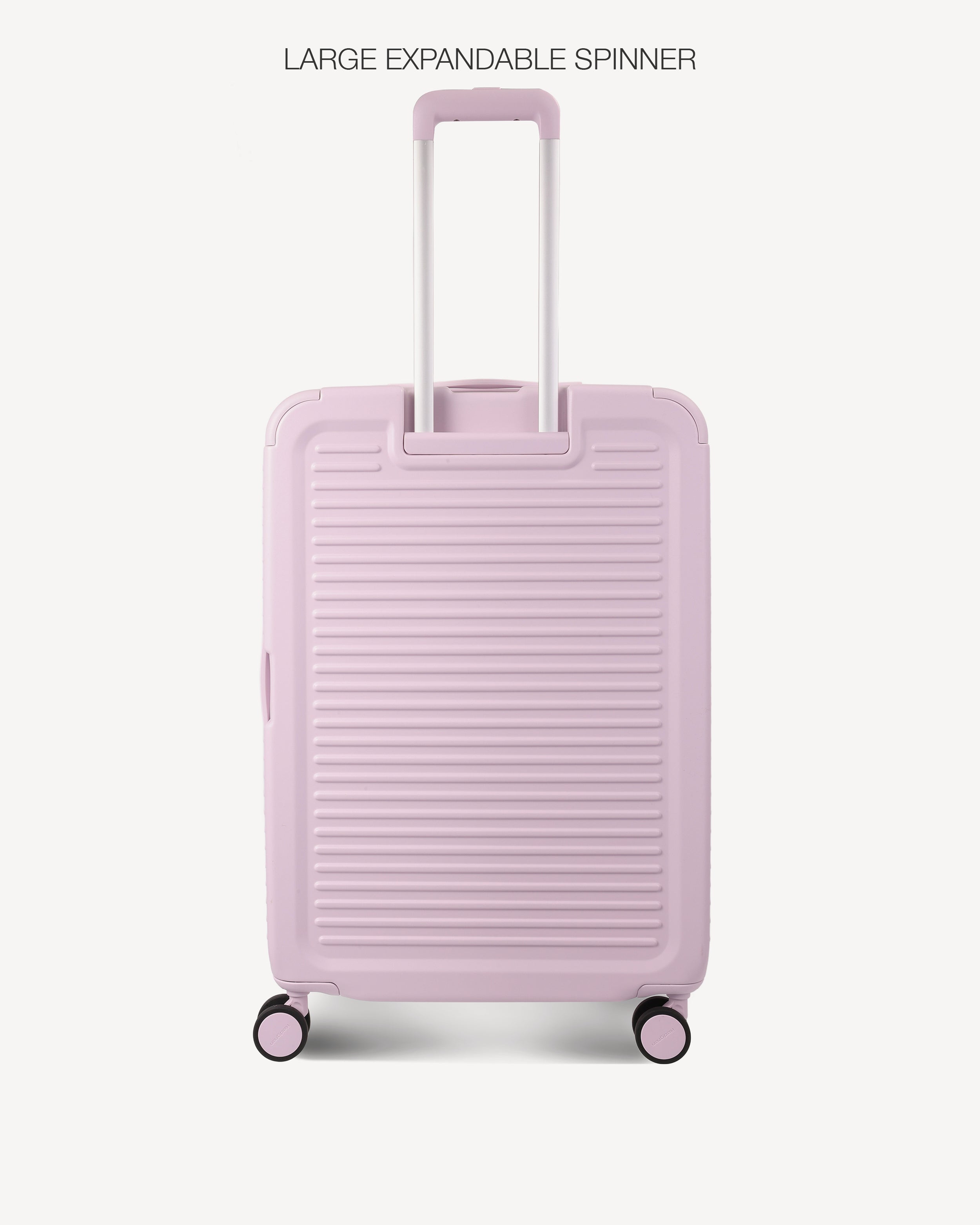 A light pink hard-shell spinner suitcase with a textured horizontal ribbed design, featuring an extended telescopic handle and four wheels, shown against a plain off-white background with the text 'LARGE EXPANDABLE SPINNER' at the top.