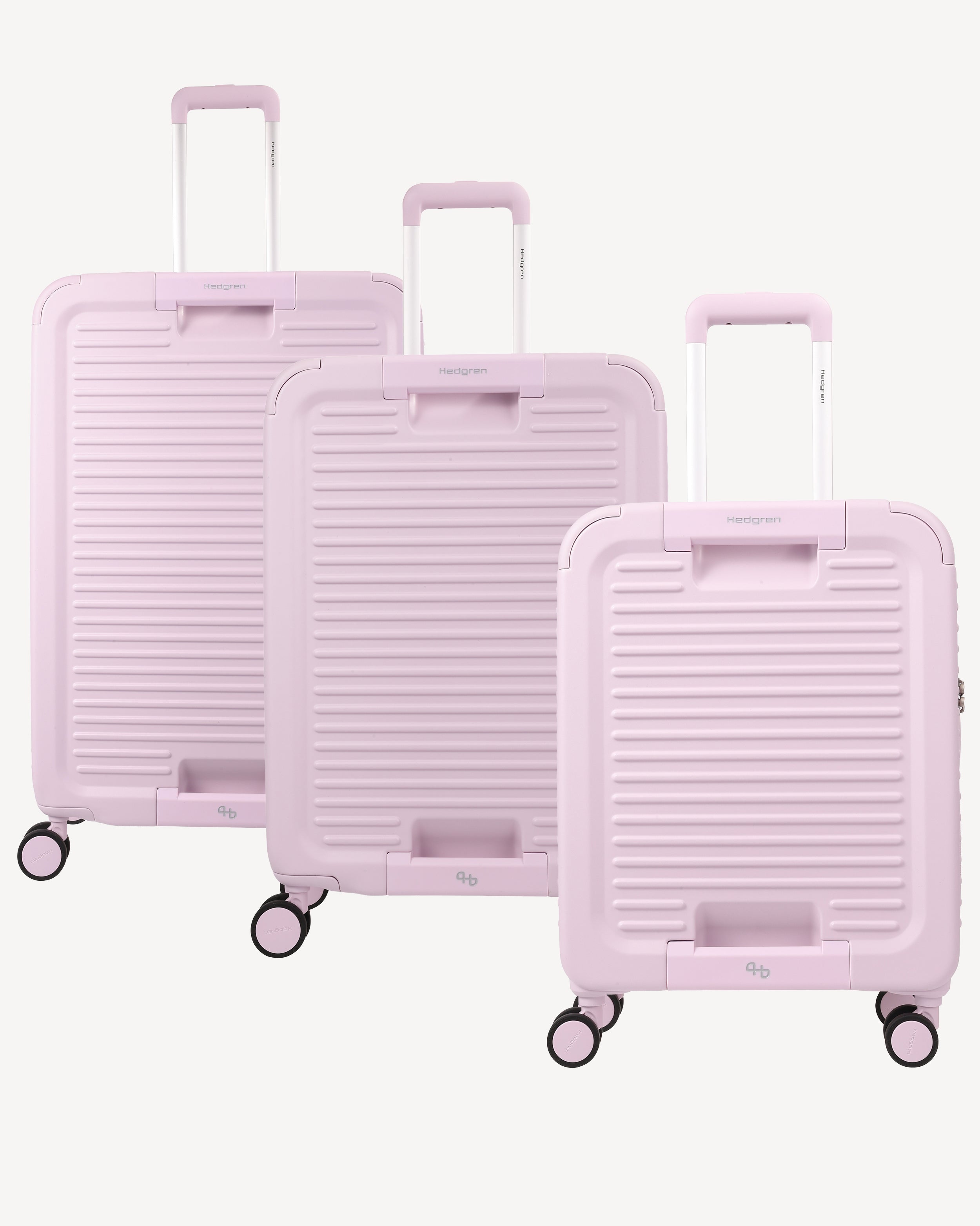Three pastel pink hard-shell spinner suitcases of different sizes arranged in a staggered row against a light off-white background. The suitcases feature a ribbed texture, telescoping handles, and four wheels each.